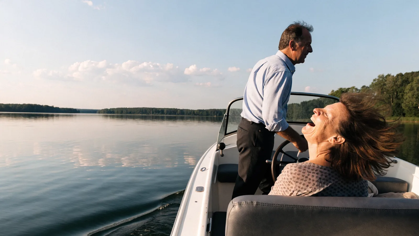 Ein Paar auf dem eigenen Motorboot: er steuert, sie lacht mit wehenden Haaren, ein See im Sommerlicht