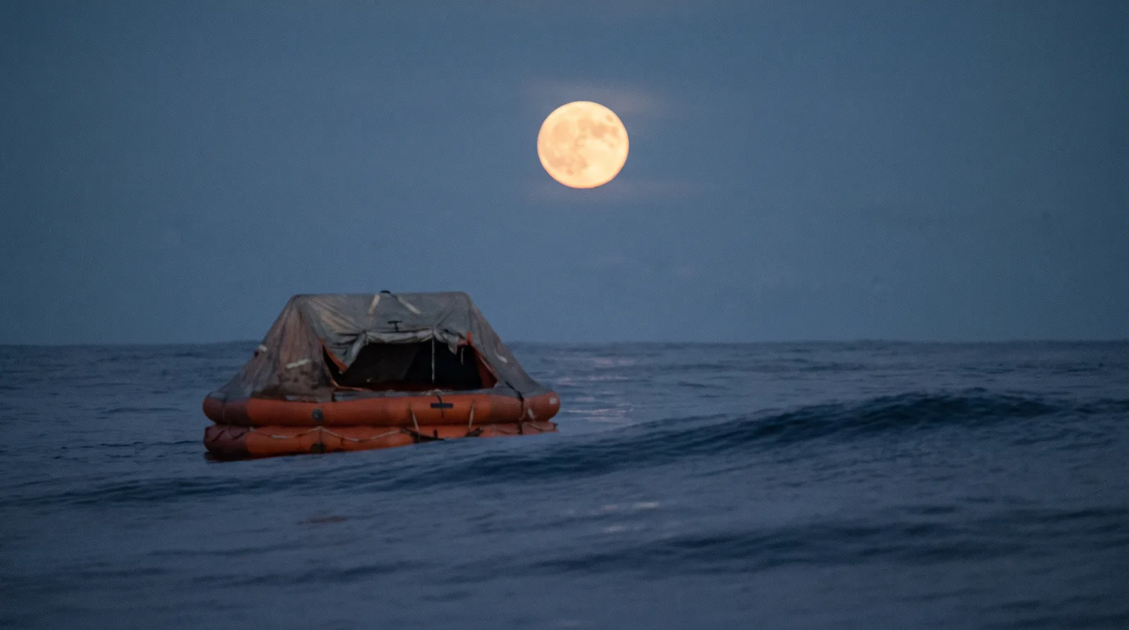 Eine orange Rettungsinsel treibt bei Vollmond allein auf dem offenen Pazifik