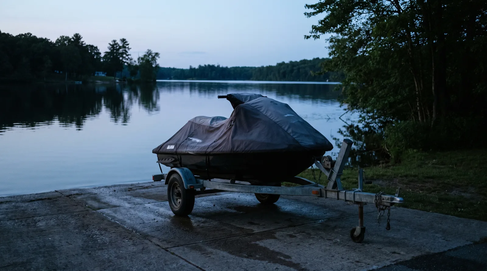 Ein Jetski auf einem Trailer an einer betonierten Slipanlage an einem See zur blauen Stunde.