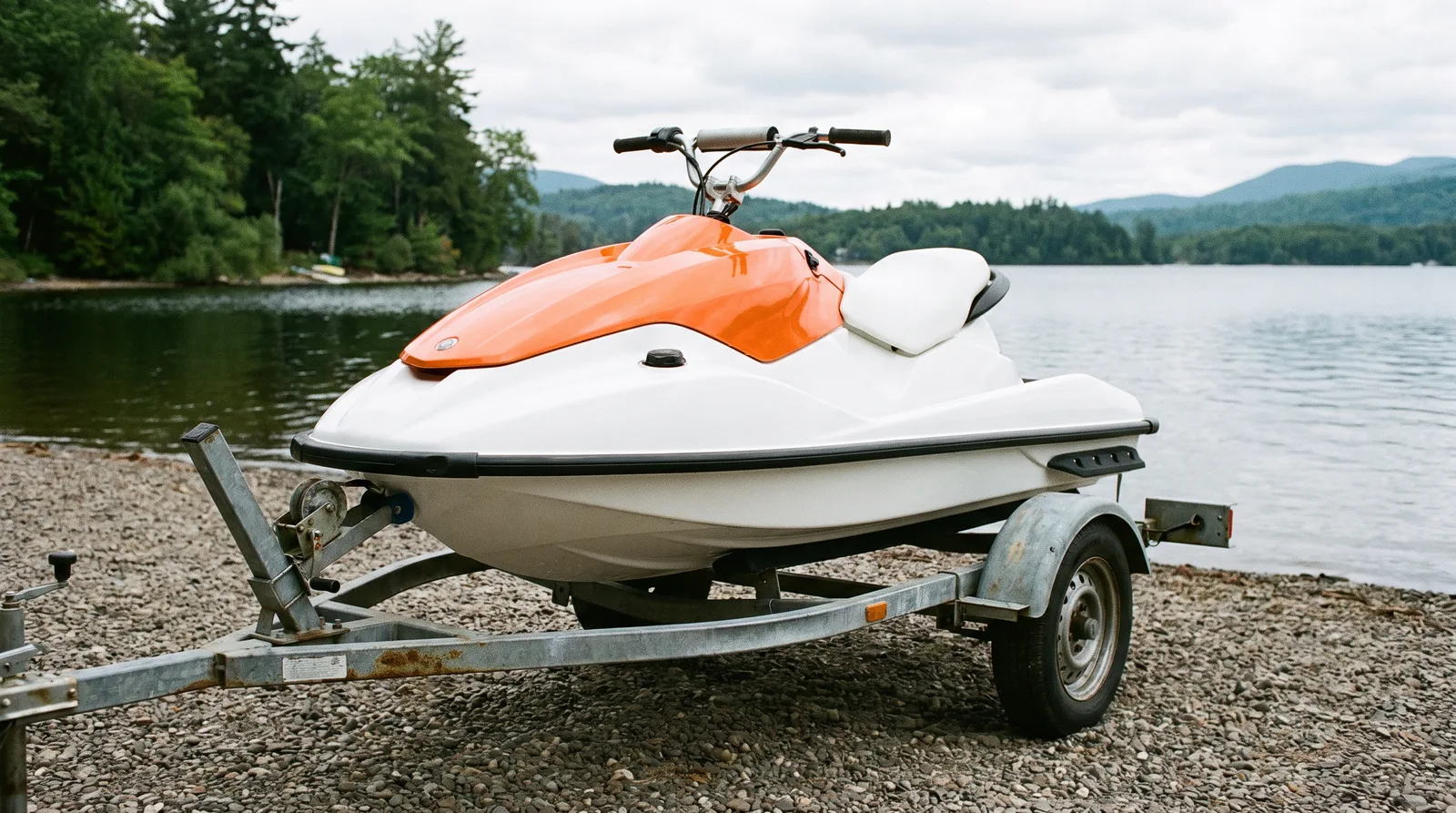 Kleiner Jetski in Orange und Weiß mit hohem Lenker auf einem Trailer am Seeufer.