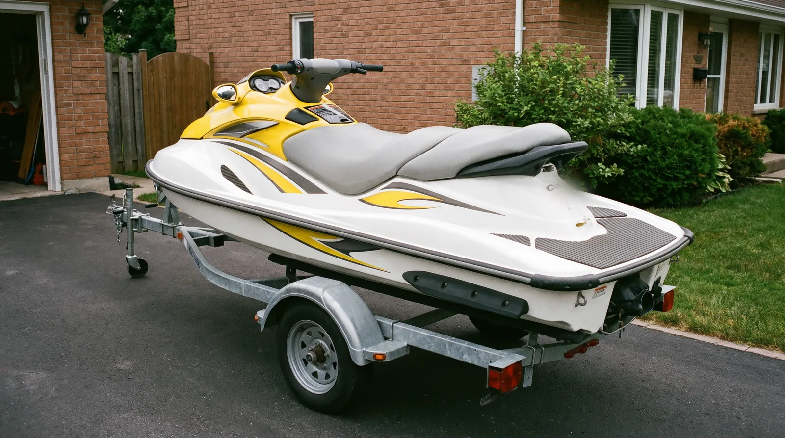 Tourenjetski in Weiß und Gelb auf einem Trailer in einer Einfahrt.