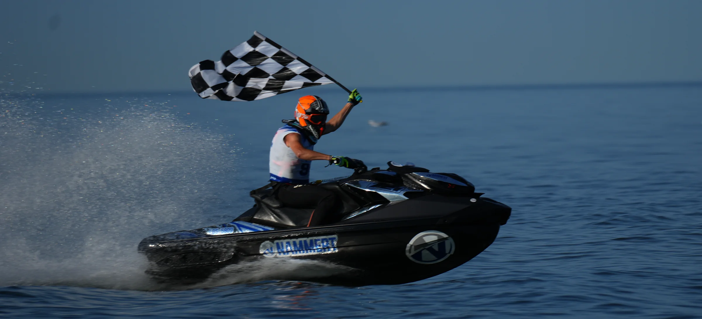 Jetski-Fahrer mit NAMMERT Logo und Startnummer schwenkt im Ziel die Zielflagge