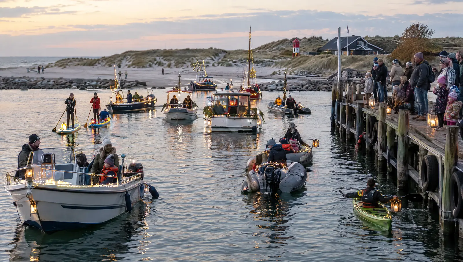 Mit Lichterketten geschmückte Boote, Kajaks und SUPs im Hafen, Zuschauer auf dem Steg