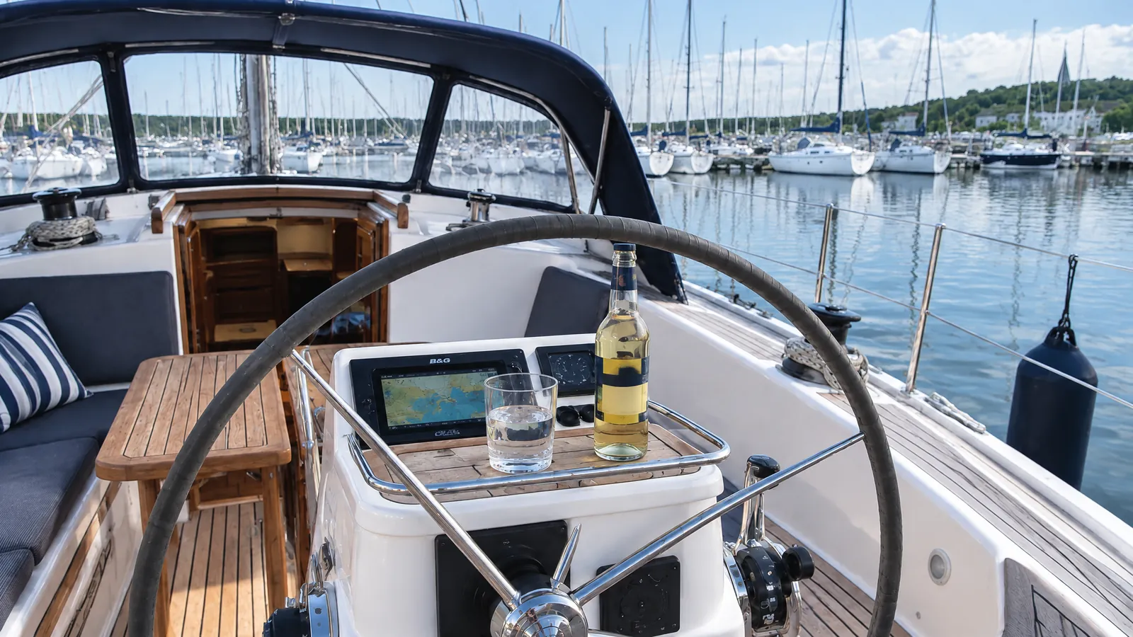Blick in das sonnenbeschienene Cockpit einer Segelyacht, neben dem Steuerstand ein Glas Wasser und ein alkoholfreies Getränk