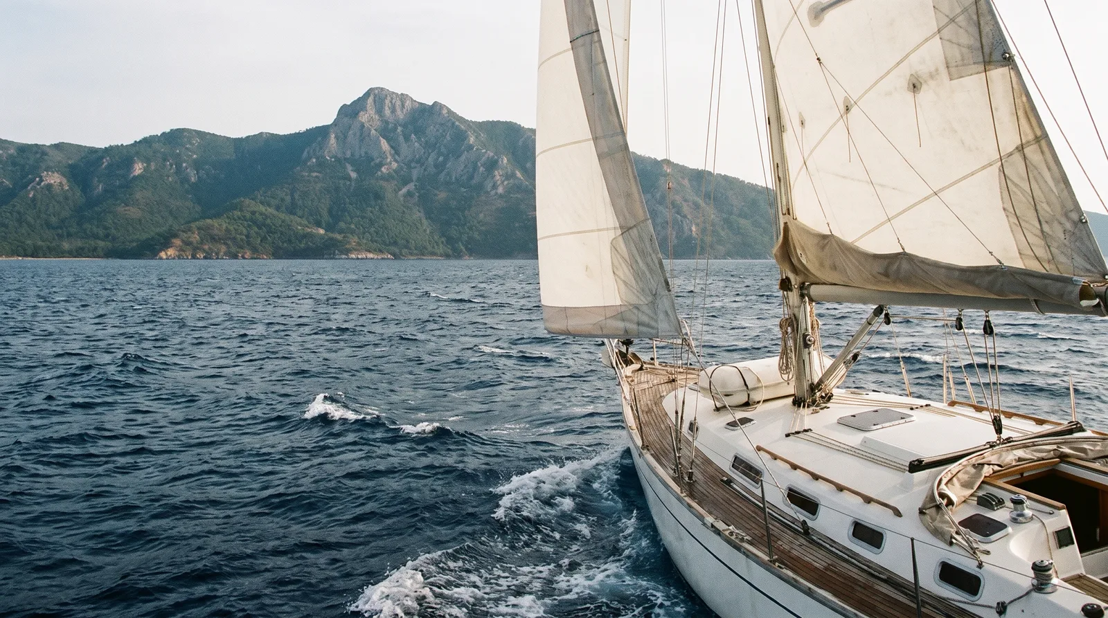 Segelyacht unter Segeln vor einer bewaldeten Halbinsel mit hohem Berggipfel in der Nordägäis