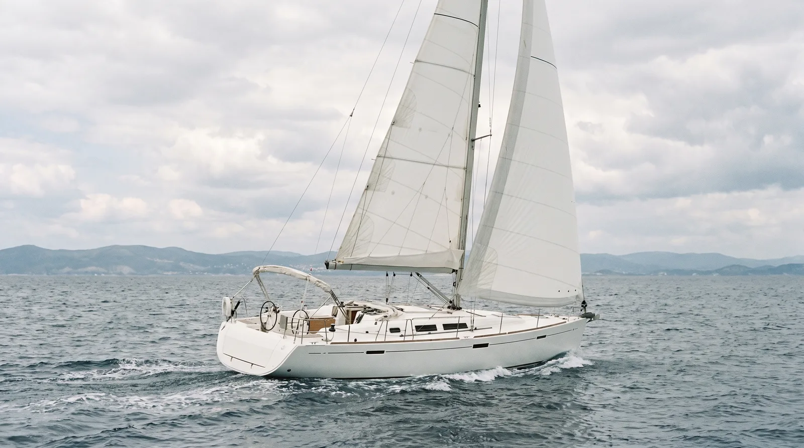 Weiße Charteryacht unter vollen Segeln auf offenem Wasser mit fernem Küstenstreifen