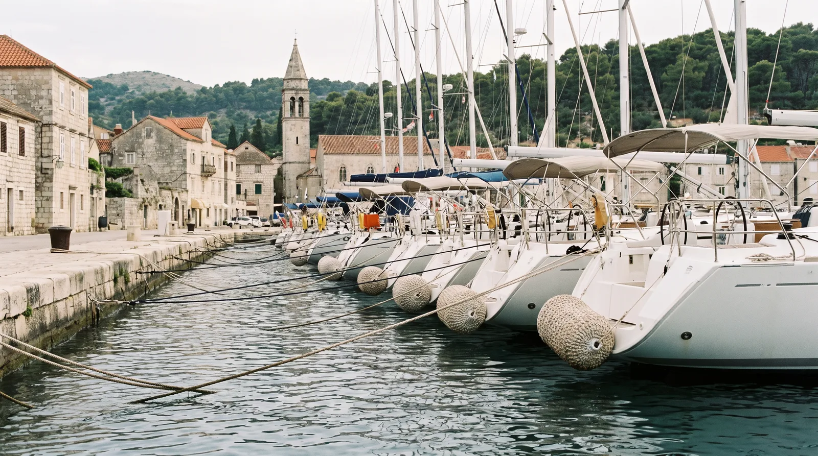 Charteryachten mit dem Heck zur Pier in einem Hafen mit alten Steinhäusern