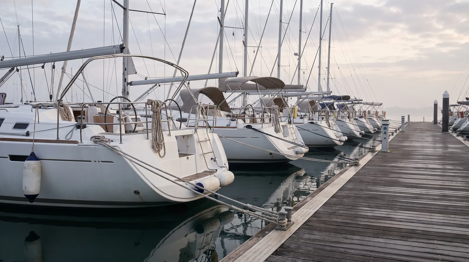 Charteryachten liegen mit dem Heck in einer Reihe am Steg einer Marina, frühes Licht