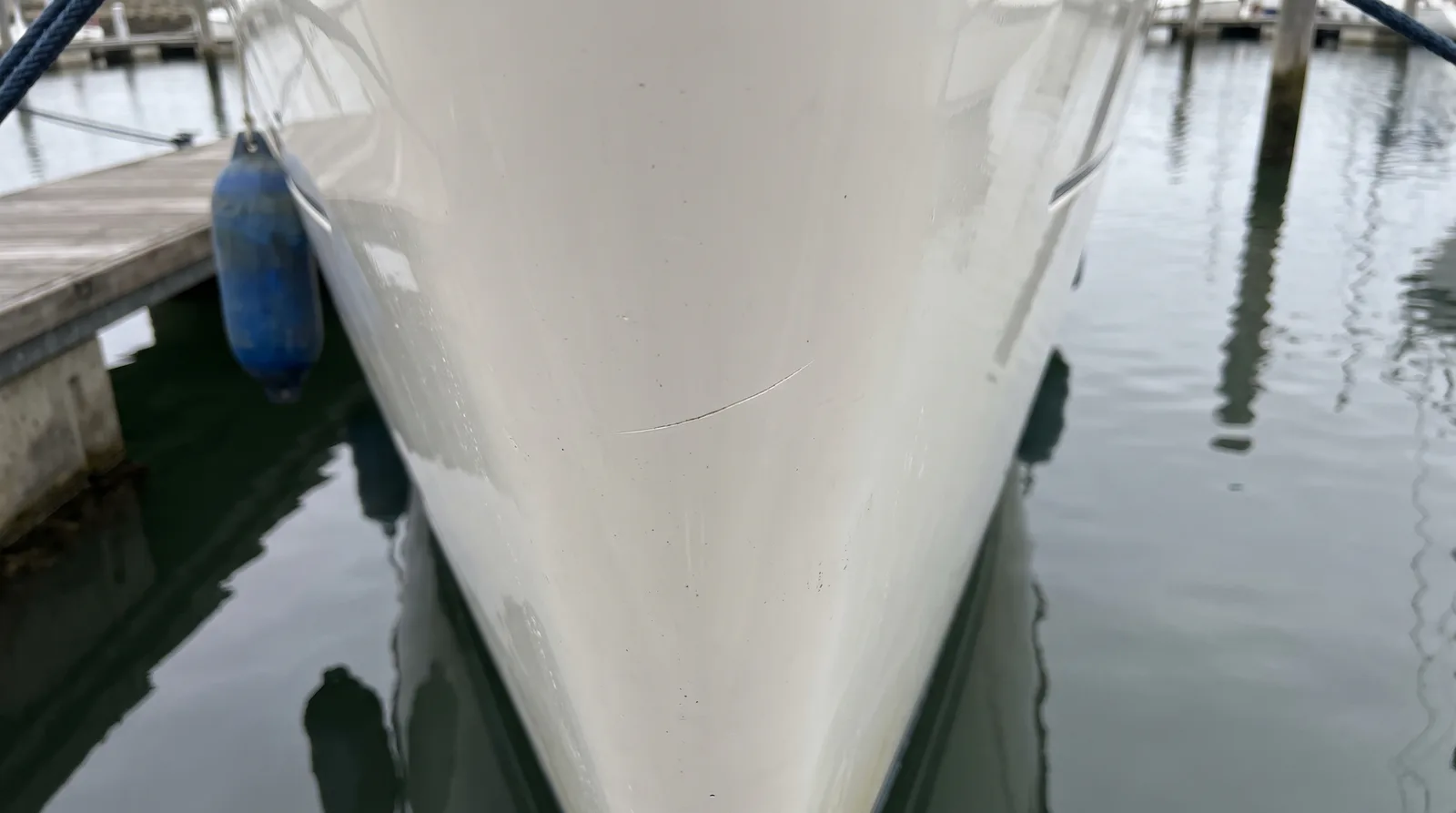 Kratzer im weißen Gelcoat am Bug einer Yacht, daneben ein Fender am Steg