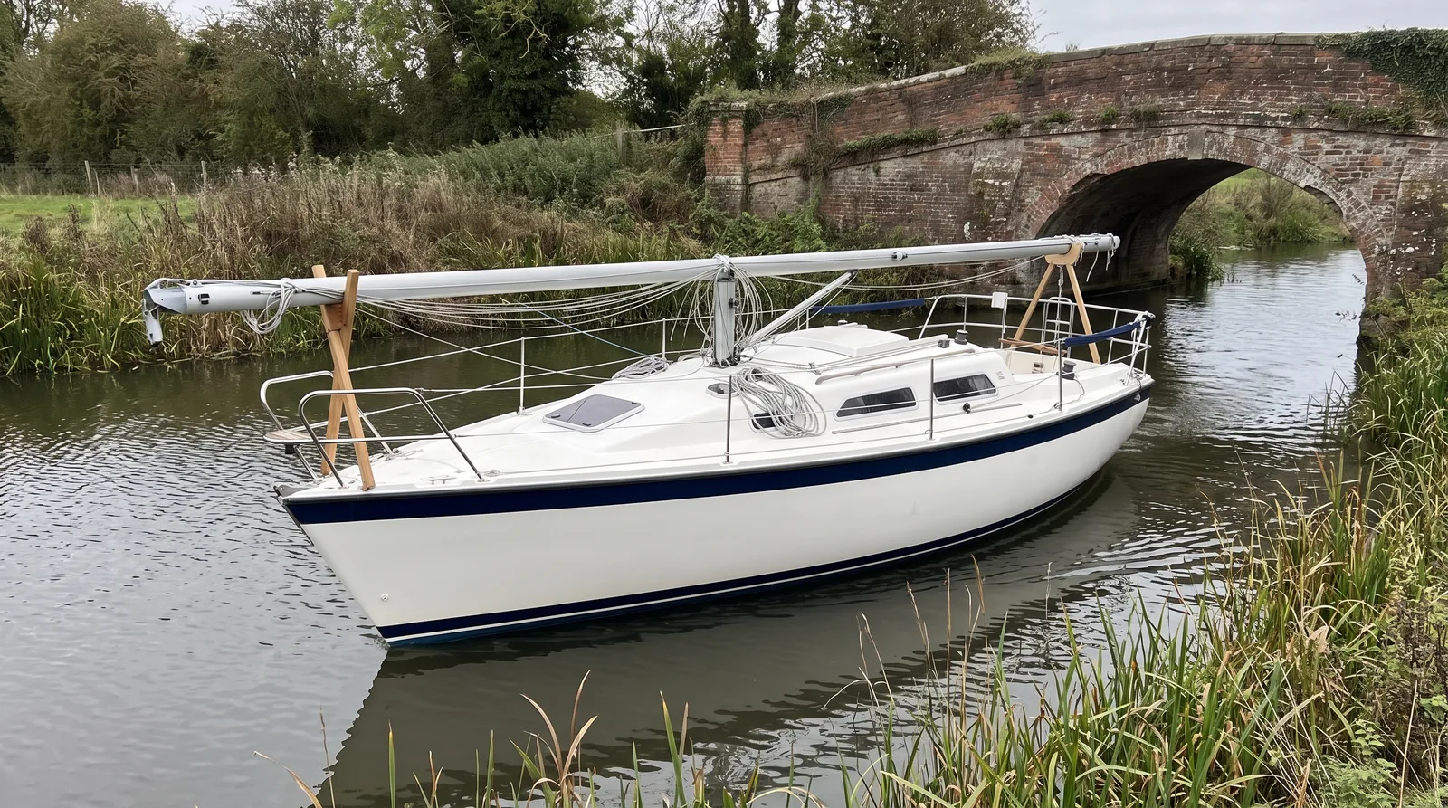 Segelyacht mit gelegtem Mast auf Holzböcken auf einem Fluss vor einer alten Ziegelbrücke