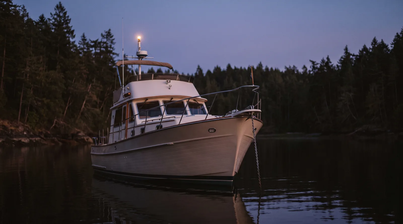 Gepflegte Motoryacht vor Anker in einer geschützten Bucht zur blauen Stunde mit weißem Ankerlicht und Ankerkette am Bug
