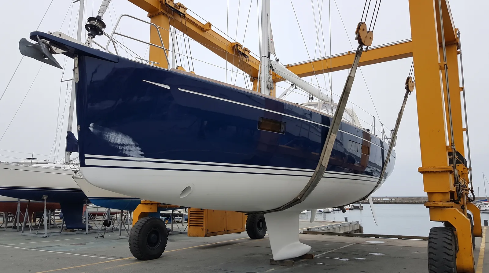 Gepflegte blaue Segelyacht hängt im Travellift einer Werft und wird zur Reparatur an Land geholt