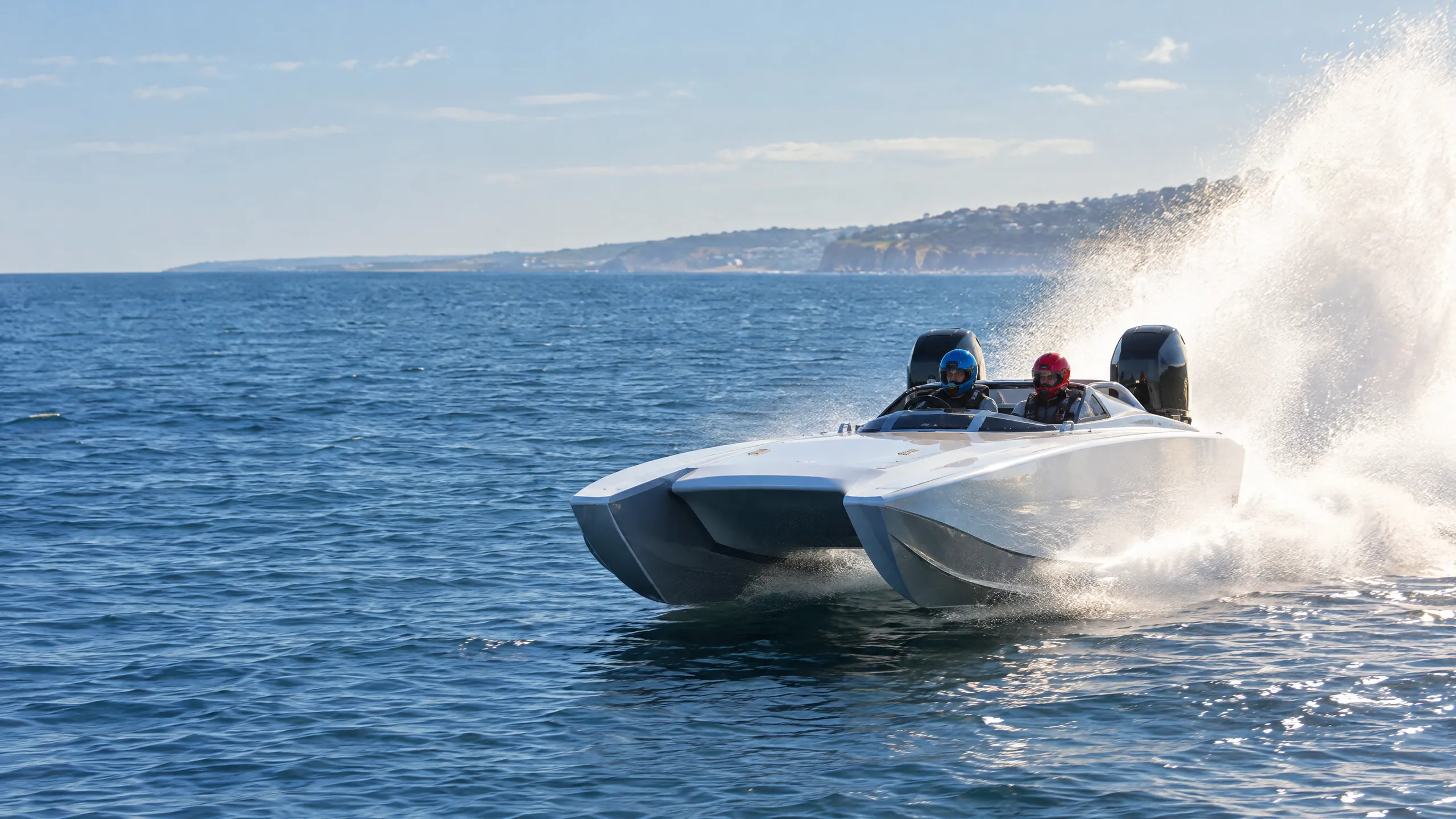 Ein weißer Rennkatamaran mit zwei Außenbordern fliegt über das Meer, zwei Fahrer mit Helm, dahinter hohe Gischt