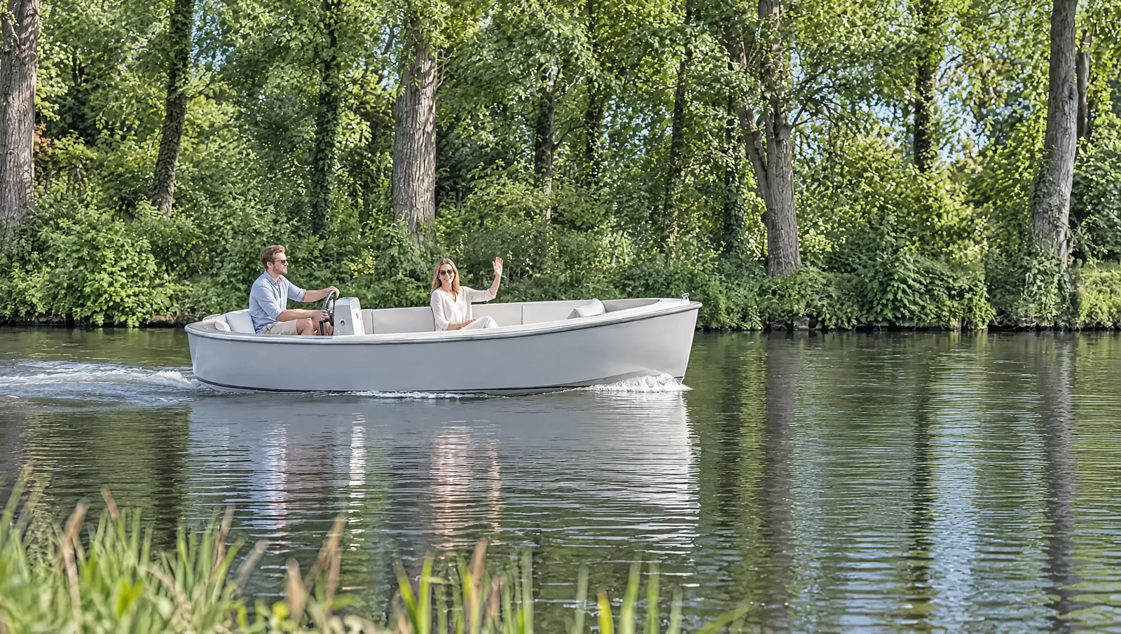 Hellgraues Elektroboot gleitet im Sonnenlicht über den Kanal, er sitzt am Steuer, sie lacht und winkt ans Ufer